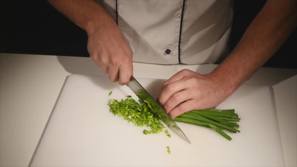 Το πράσινο κρεμμύδια με ένα μαχαίρι κόβουμε στο Διοικητικό Συμβούλιο. Πράσινο κοπής χωρίς χέρια στο πλαίσιο. Σεφ κόβει τα υλικά για τη σούπα. Τεμαχισμένο πράσινο. Μαγείρεμα των τροφίμων. Ψιλοκόβουμε τα υλικά για τη σαλάτα — Αρχείο Βίντεο