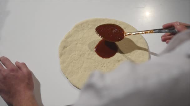 Chef extendiendo salsa de tomate en masa de pizza con un cucharón de metal en el restaurante de pizza — Vídeo de stock