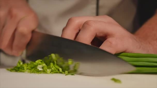 Το πράσινο κρεμμύδια με ένα μαχαίρι κόβουμε στο Διοικητικό Συμβούλιο. Πράσινο κοπής χωρίς χέρια στο πλαίσιο. Σεφ κόβει τα υλικά για τη σούπα. Τεμαχισμένο πράσινο. Μαγείρεμα των τροφίμων. Ψιλοκόβουμε τα υλικά για τη σαλάτα — Αρχείο Βίντεο