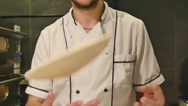 Young guy in chef uniform spinning and tossing pizza dough in restaurant kitchen in slow motion — Stock Video