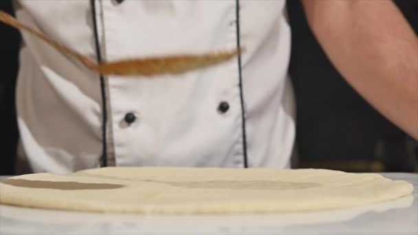 Chef-kok strooit tomatensaus op pizza deeg met een metalen lepel in pizza restaurant — Stockvideo