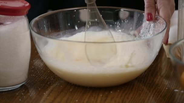 Young woman prepares dough mixing ingredients in the the bowl using whisk in the kitchen. Homemade food. Slowmotion shot — Stock Video