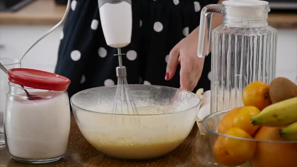 Молода жінка готує інгредієнти для змішування тіста в мисці, використовуючи вуса на кухні. Домашня їжа. Постріл уповільнення — стокове відео
