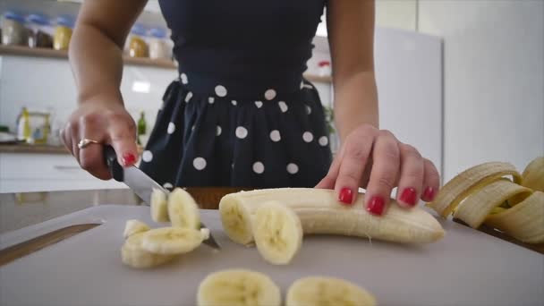 여자 가정 부엌에 나무로 되는 부엌 보드에 바나나를 슬라이스. 요리 음식 집. 부엌에서 가정 분위기 — 비디오
