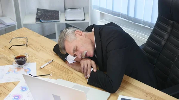 Tired businessman with laptop falling asleep in office