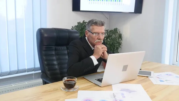 Пожилой бизнесмен, работающий с компьютером в современном офисе — стоковое фото