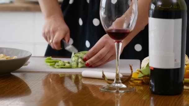 Muchacha atractiva sentada en la mesa de la cocina y rebanando kiwi — Vídeos de Stock