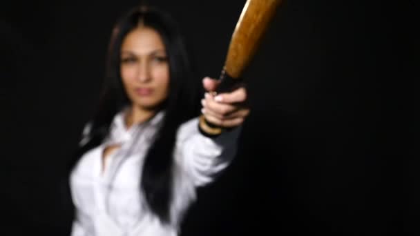 Young beautiful girl looking at camera brutally, holding bat over black background. slow motion. selective focus — Stock Video