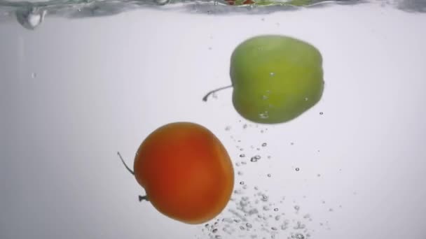 Яблоко и помидор падают в воду в аквариуме — стоковое видео