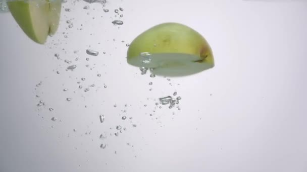 Jumătate din măr cade în apă pe fundal alb — Videoclip de stoc
