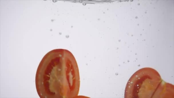 Нарезанные помидоры падают в воду на белом фоне — стоковое видео