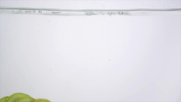 Rodajas de Kiwi cayendo en el agua. Piezas de Kiwi cae bajo el agua sobre fondo blanco. Fresh Kiwi Fruit Plunging And Splashes Water. Burbujas de aire de agua — Vídeo de stock