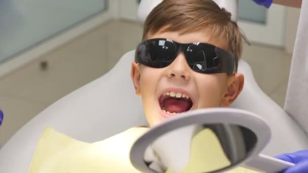 Пациент сидит на стоматологическом стуле в кабинете детского стоматолога — стоковое видео