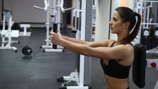 Mujer entrena brazos y hombros en simulador en gimnasio — Vídeo de stock