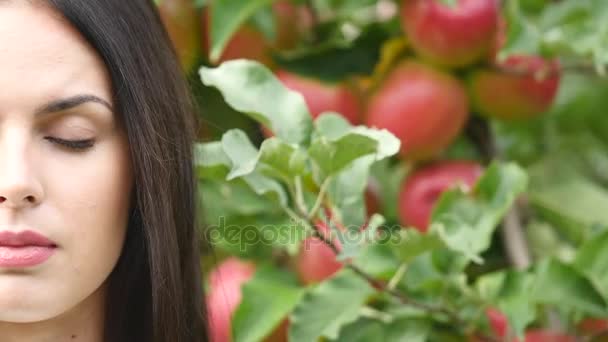 Giovane donna vestita con un vestito bianco che si gira e posa davanti alla telecamera davanti al sole nel giardino fiorito di melo. vicino — Video Stock