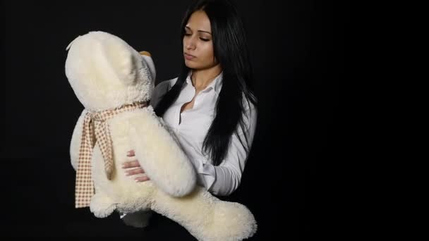 Ένα υπέροχο κορίτσι αγκαλιάζει ένα χαριτωμένο αρκουδάκι. Στενή-up shot, στούντιο σε μαύρο φόντο — Αρχείο Βίντεο