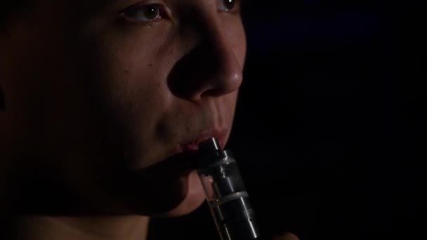 Человек, курящий электронный сигаретный пар на черном фоне — стоковое видео
