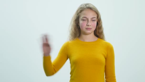 Chica de pie y agitando su mano sobre un fondo blanco en el estudio — Vídeo de stock