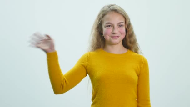 Menina de pé e acenando com a mão em um fundo branco no estúdio — Vídeo de Stock