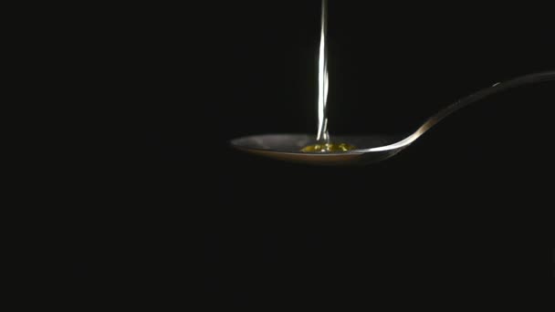 Honig tropft aus dem rostfreien Teelöffel auf schwarzem Hintergrund — Stockvideo