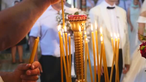 Mão das mulheres segura e coloca uma vela na igreja. Muitas velas acesas — Vídeo de Stock