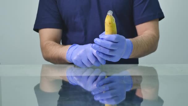 Una mano de hombre poniéndose un condón en un plátano. Concepto de sexo seguro y prevención de enfermedades de transmisión sexual — Vídeo de stock