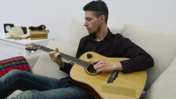 Genç adam bir kanepede oturan ve gitar çalmak — Stok video