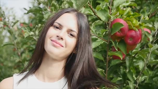 Jonge vrouw gekleed in een witte jurk draaien en poseren op de camera voor de zon in de appelboom bloeide tuin. Close-up — Stockvideo