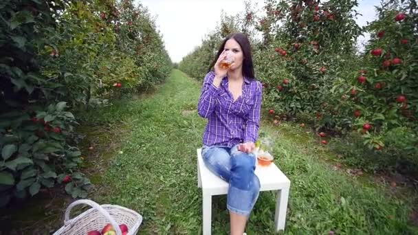 Bella ragazza giardiniere si siede sul tavolo di legno e bere succo di frutta. rallentatore — Video Stock