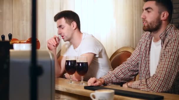 Zwei befreundete junge Männer sitzen in der Bar und unterhalten sich beim Biertrinken — Stockvideo