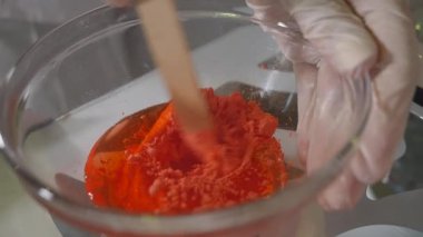 Bir güzellik uzmanı yüz maskesini fırçayla karıştırır. Genç kozmetikçi kozmetik kremini küçük bir kapta karıştırıyor. Kozmetik kremi karıştırılıyor