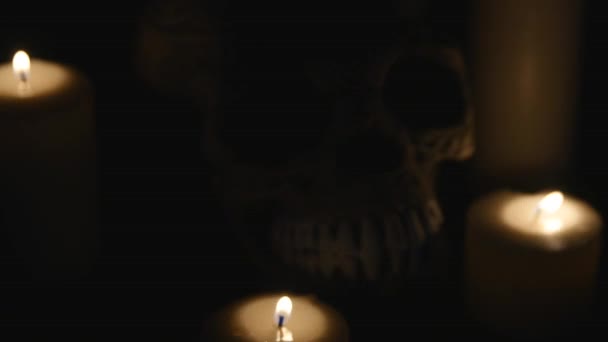 Cuatro velas encendidas y un cráneo sobre un fondo negro. de cerca — Vídeos de Stock