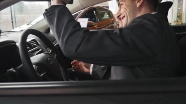 Bir adam iç araç olup olmadığını denetler. Otomatik iş, araba Satılık, teknoloji ve insan kavramı - auto göstermek ya da salon araba satıcısı ile mutlu erkek. Bir satıcı motor gösterisi ile genç adam