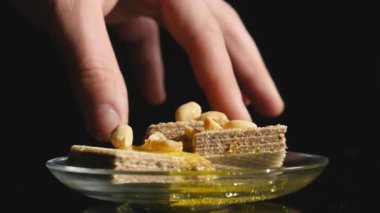 siyah bir zemin üzerine bir kasede waffle bal ve fındık ile el alır