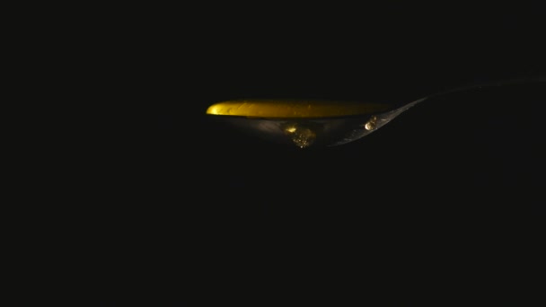 Honig fließt aus dem Löffel vor schwarzem Hintergrund — Stockvideo