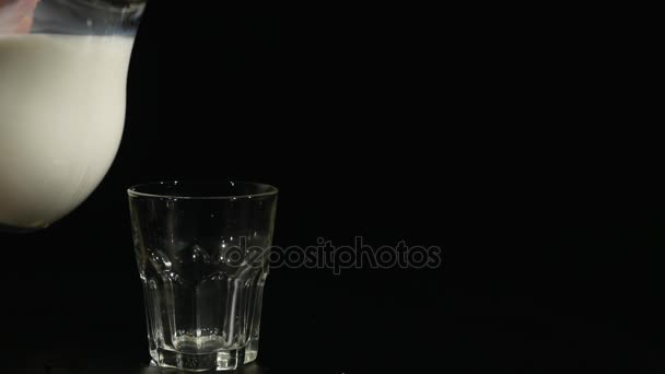 Milch im langen Strom in ein Glas auf schwarzem Hintergrund gießen — Stockvideo