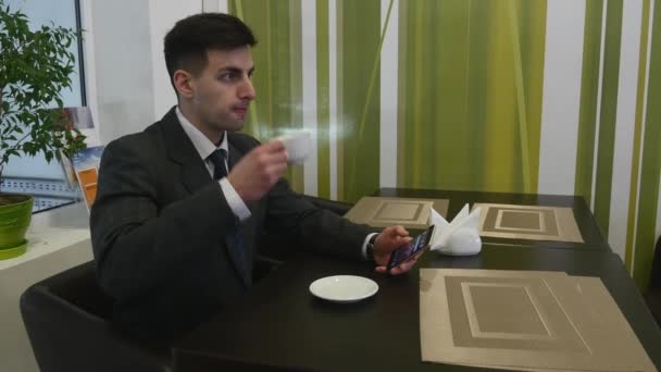 Ένας άνδρας κάθεται σε ένα τραπέζι στο καφενείο και χρησιμοποιεί το τηλέφωνο. Το τηλέφωνο στο αριστερό του χέρι — Αρχείο Βίντεο