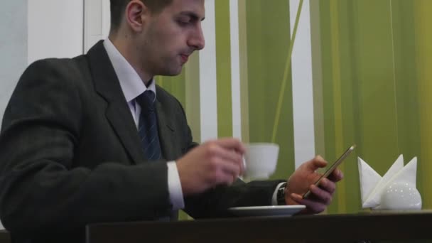 Un hombre se sienta en una mesa en el café y usa el teléfono. El teléfono en su mano izquierda — Vídeos de Stock