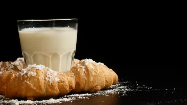 Vidro de leite com croissant girar sobre um fundo preto — Vídeo de Stock