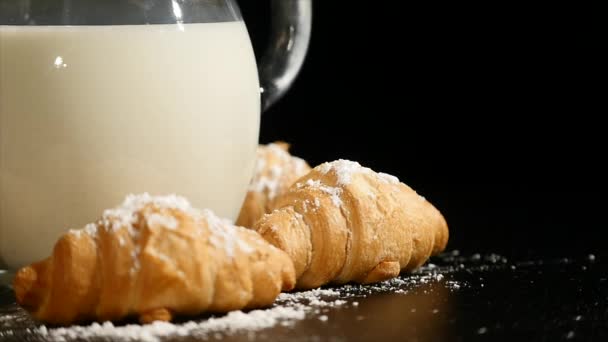 Jarra de leche con croissant girar sobre un fondo negro — Vídeo de stock