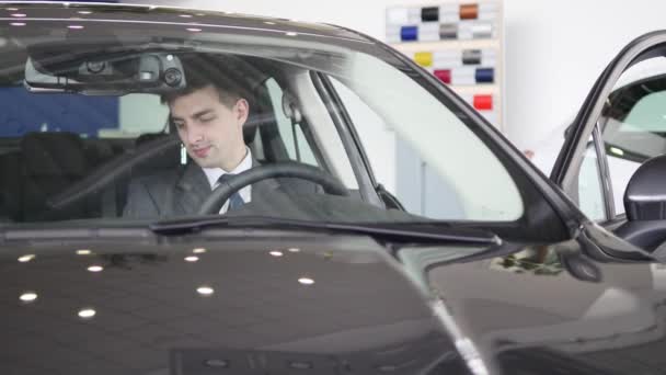 Un bărbat inspectează interiorul vehiculului. Afaceri auto, vanzari auto, tehnologie si conceptul de oameni - barbat fericit cu dealer auto in auto show sau salon. Tânăr cu un vânzător într-un salon auto — Videoclip de stoc