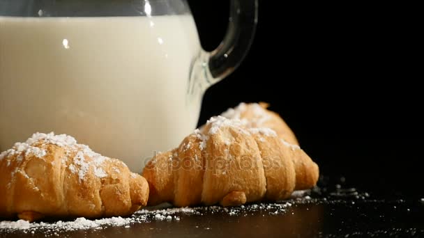 Jarra de leche con croissant girar sobre un fondo negro — Vídeos de Stock