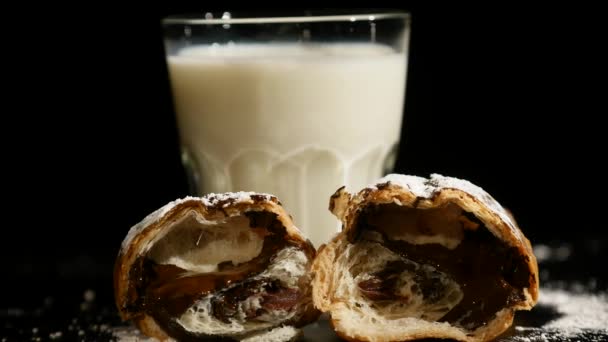 Glas Milch mit Hälften Croissant drehen sich auf schwarzem Hintergrund — Stockvideo