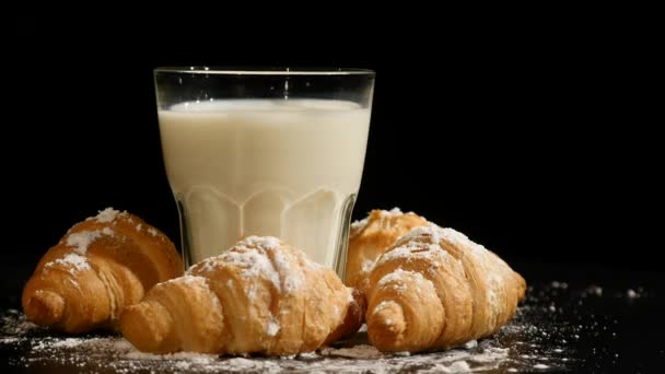 Vidro de leite com croissant girar sobre um fundo preto — Vídeo de Stock