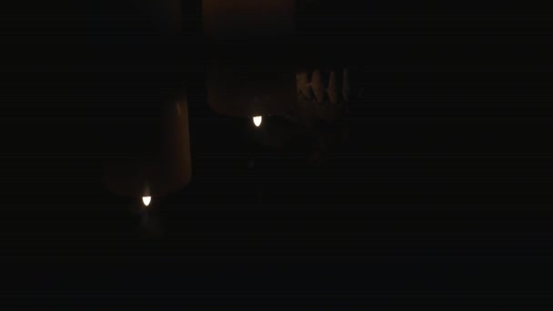 Две зажженные свечи и череп на черном фоне — стоковое видео