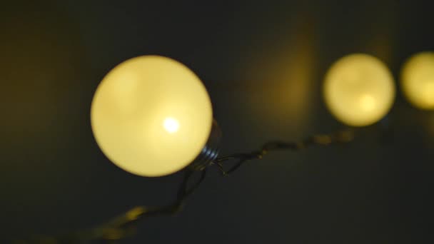 Лампочки гирлянда близко. Электрическая лампочка блеск висит на стене в качестве украшения для праздника крупным планом — стоковое видео