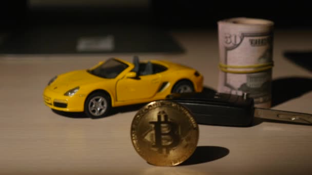 Bitcoins moedas com carro pequeno e chaves do carro e dólares torcidos — Vídeo de Stock
