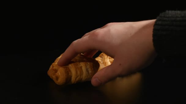 Mão leva croissant no fundo preto — Vídeo de Stock