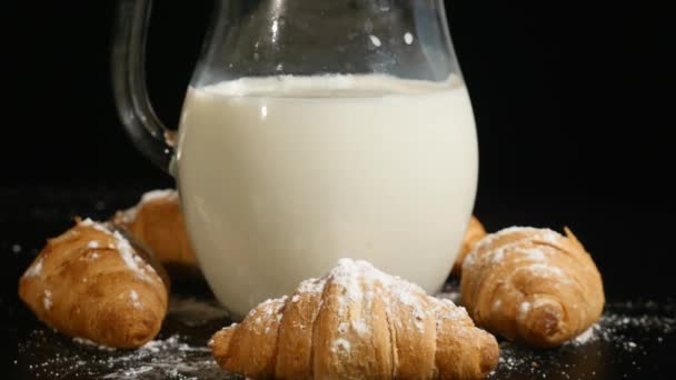 Milchkrug mit Croissant rotieren auf schwarzem Hintergrund — Stockvideo