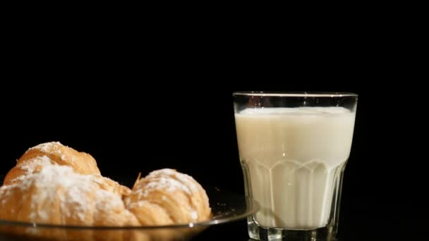 Glas Milch mit Croissant drehen sich auf schwarzem Hintergrund — Stockvideo